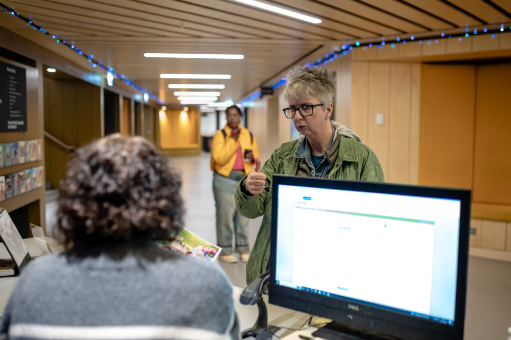 An older visitor at a customer service point gives a thumbs up to a staff member.