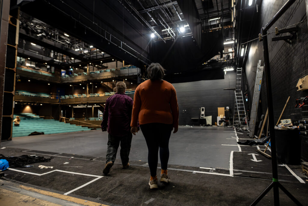 Two performers walk onto a level access stage. The edge is well-defined and the lighting avoids glare or high contrast.