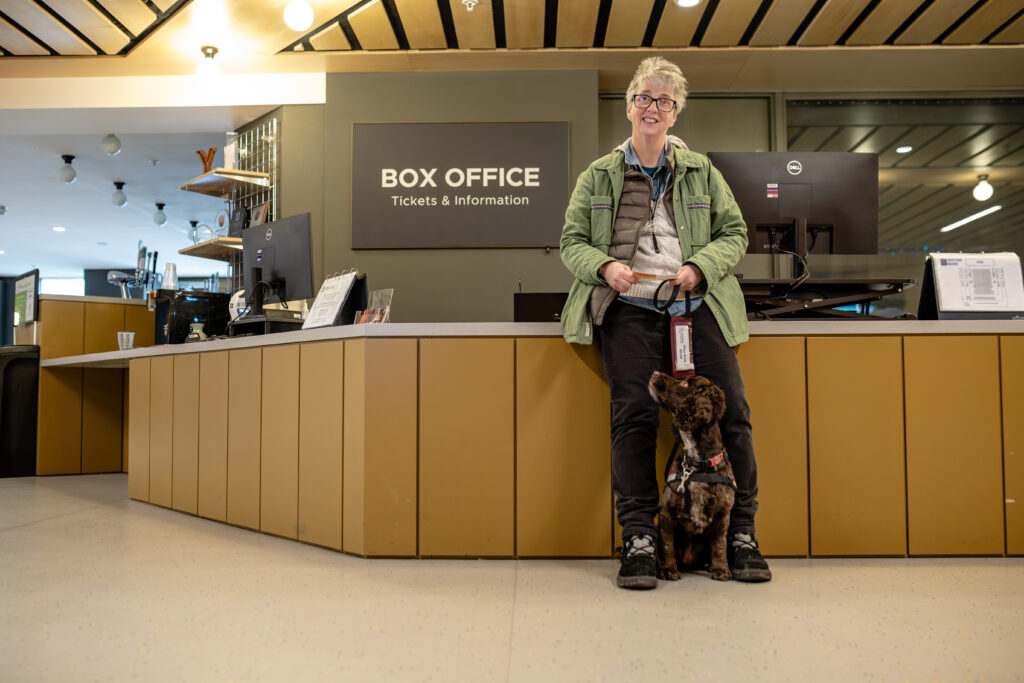 A visitor stands in front of a box office counter. A large sign shows that this is where to get tickets and information.