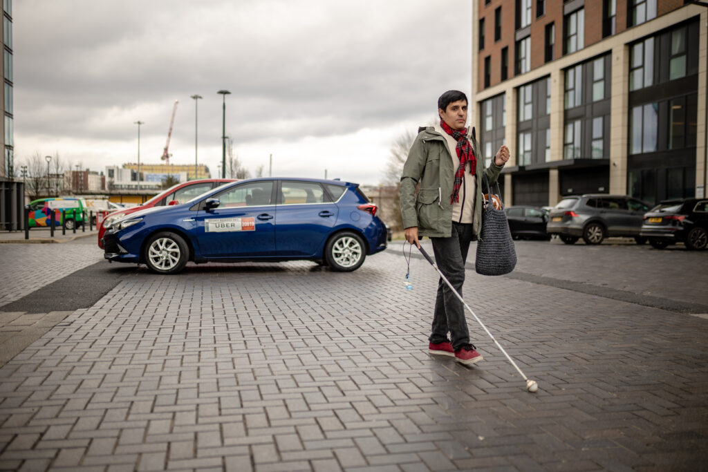 A white cane user approaches a venue after being dropped off in an area with a level, firm surface.