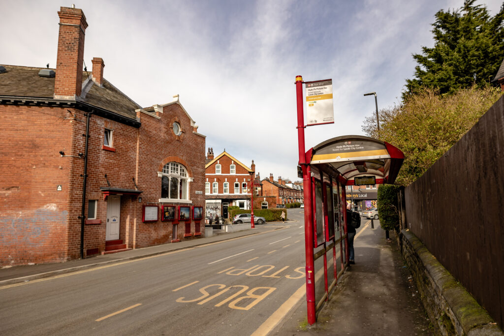 A bus stop with a shelter located close to a cinema entrance.