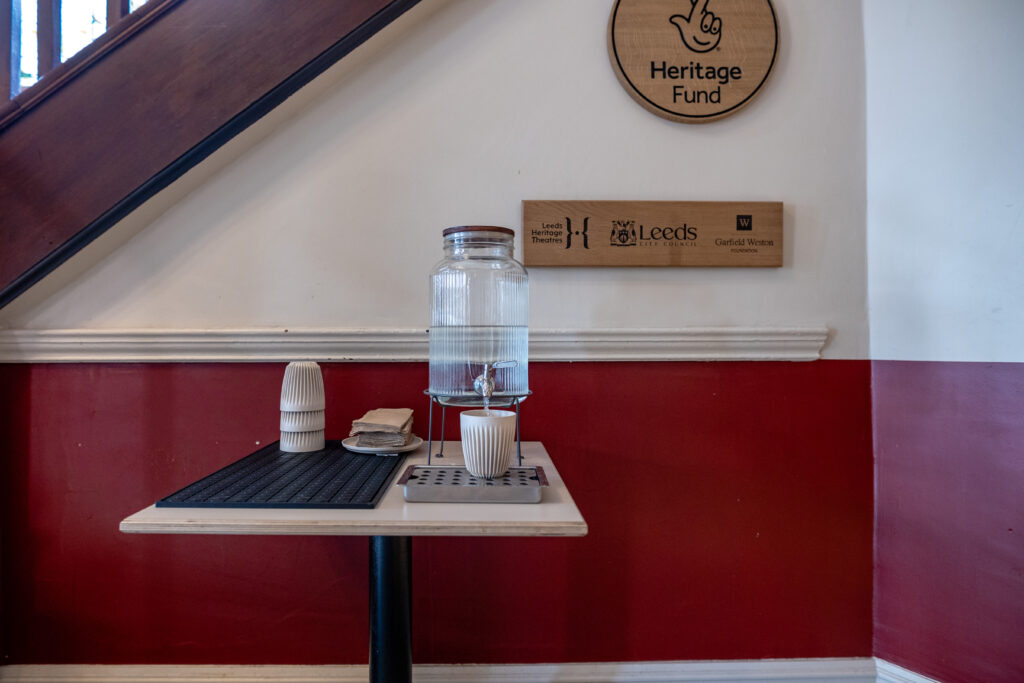 Water dispenser and rigid plastic cups on a low table with a non-slip mat.