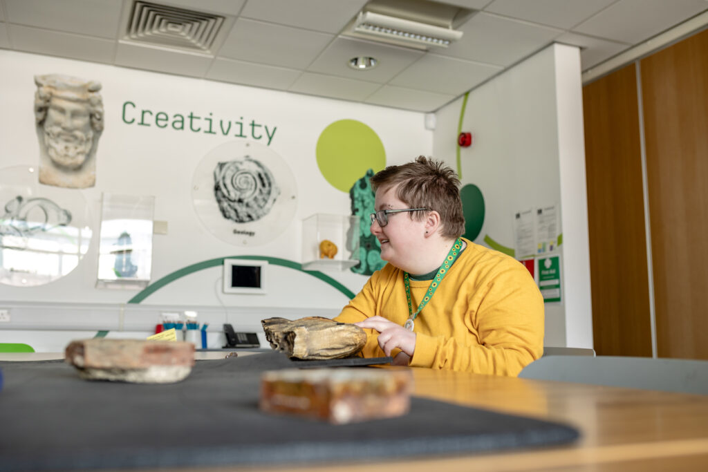 A person wearing a sunflower lanyard enjoys an activity in a calm, quiet room with good natural light and lots of seating.