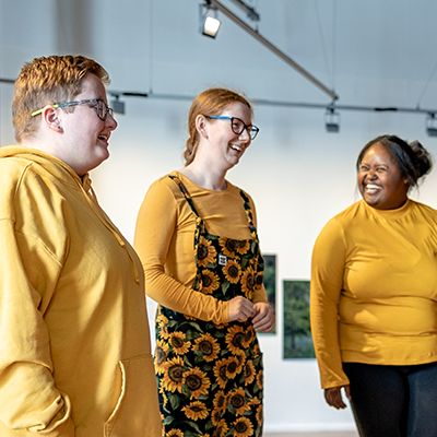 Grŵp o bobl yn chwerthin wrth fwynhau arddangosfa ffotograffiaeth mewn oriel gelf.