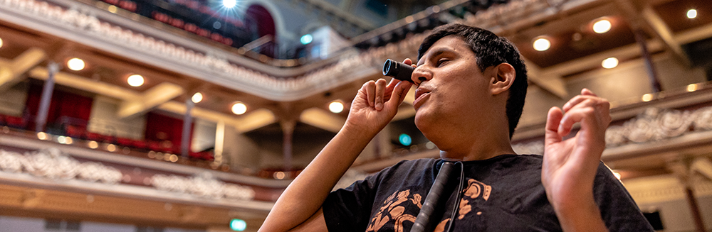 A visually impaired person in a grand theatre uses a monocular to see the stage.