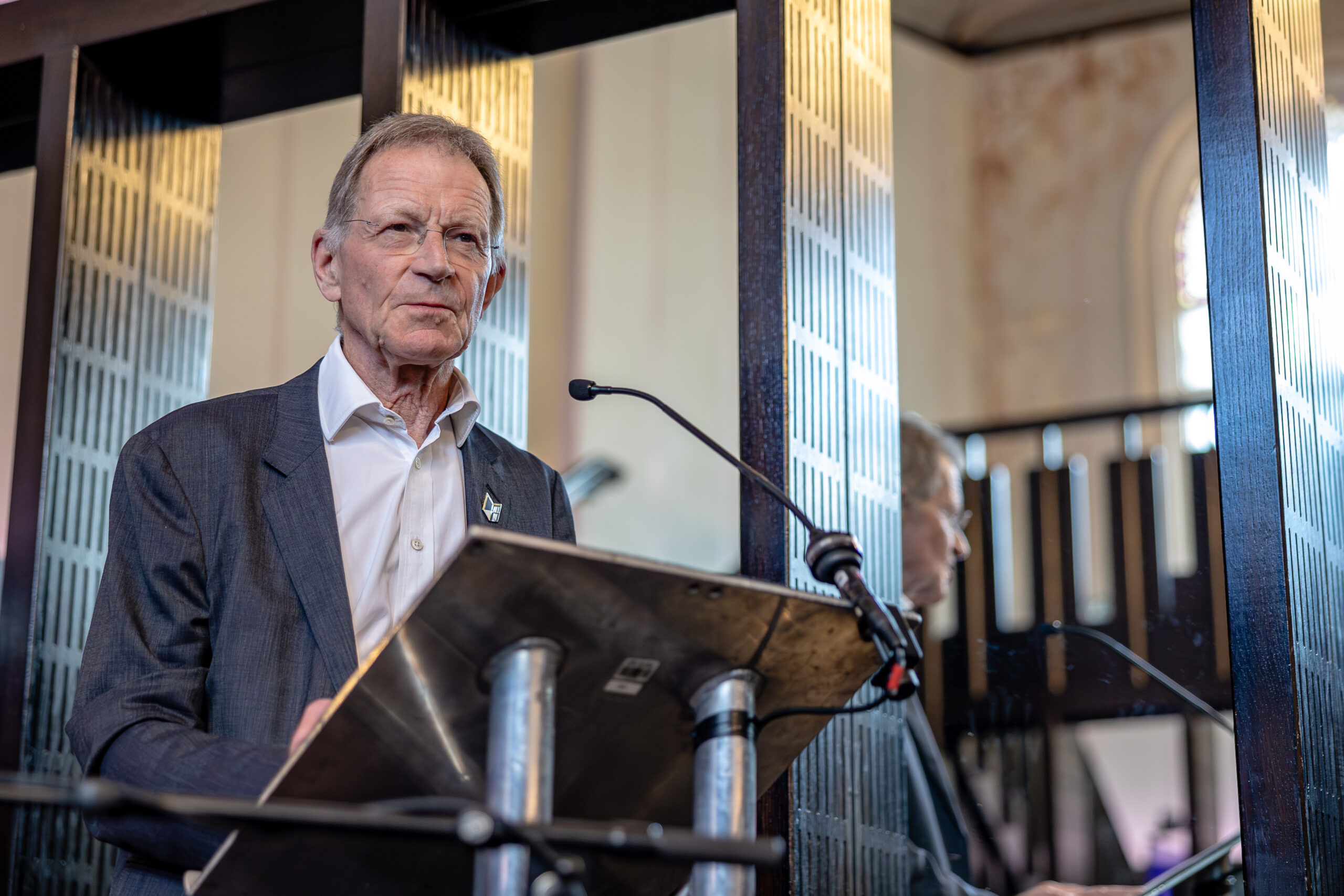 Sir Nicholas Serota stands at the lectern, looking out over the audience off camera.