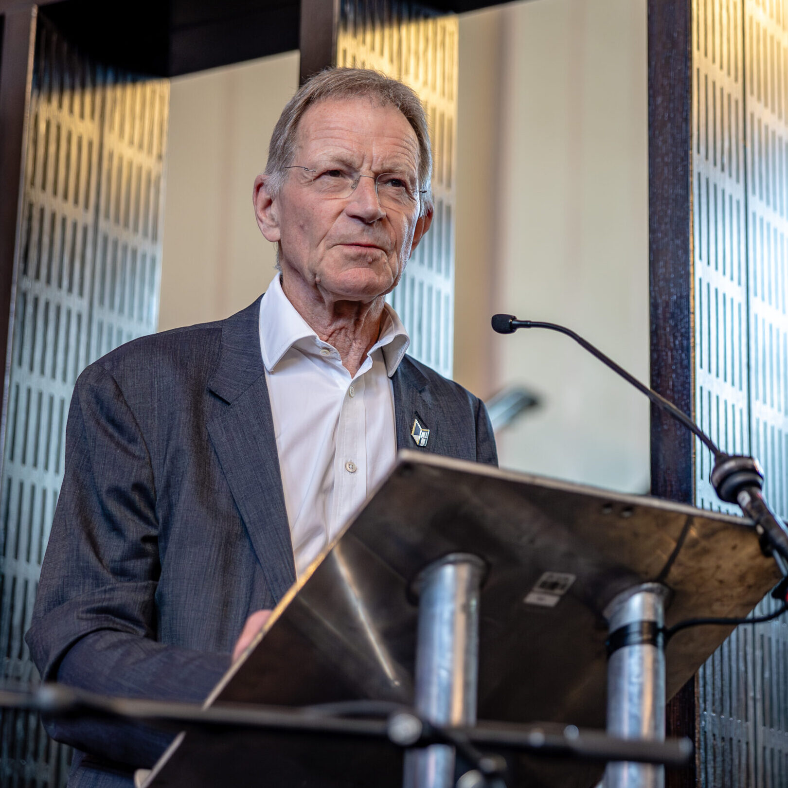 Sir Nicholas Serota stands at the lectern, looking out over the audience off camera.