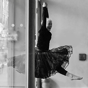 A black and white photo of Emilie leaping through the doorway of a theatre foyer in a dance pose.